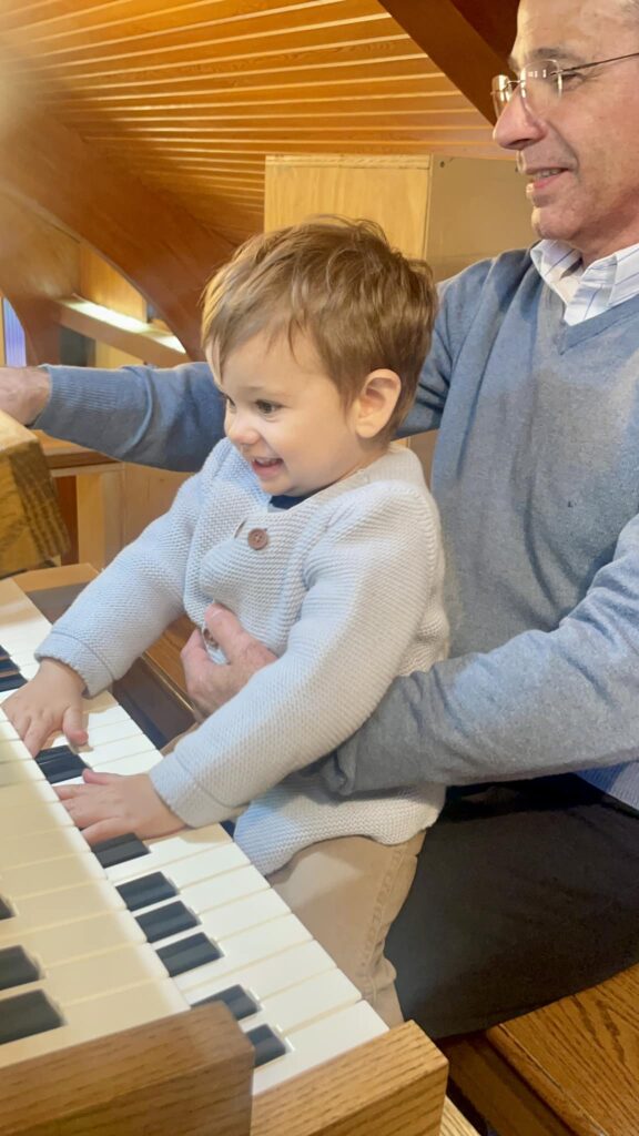 A young child at the organ keyboard, smiling, seated with his teacher.
